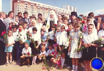 Тимошков Юрий Иванович (третий ряд, четвертый слева), мэр г. Нижневартовска, и Алексий II (в центре), Патриарх Московский и всея Руси, с учащимися православной школы на строительной площадке Храма Рождества Христова во время визита Патриарха в г. Нижневартовск с целью освящения строительства храма. Групповой снимок. 27.06.1994. 
Основание: Архивный отдел администрации города Нижневартовска. Фонд Фотодокументы. Опись 1. Дело 1167